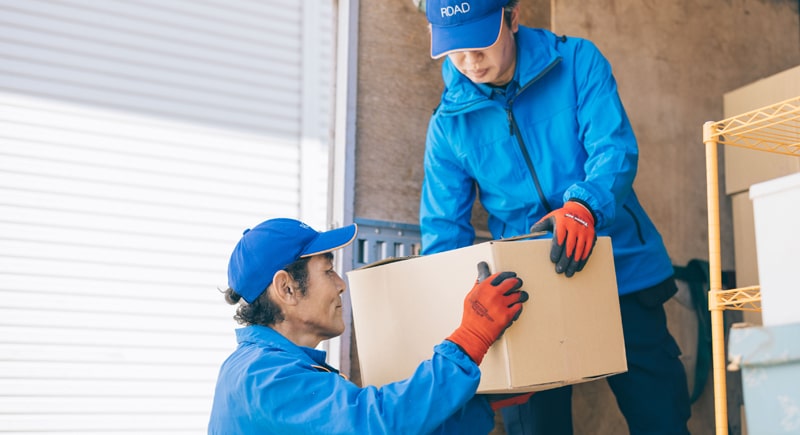 買い取った品を梱包した段ボールをトラックに積み込む遺品整理ロードの2名の男性スタッフ