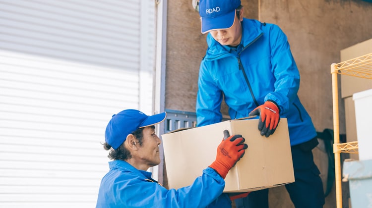 買い取った品を梱包した段ボールをトラックに積み込む遺品整理ロードの2名の男性スタッフ